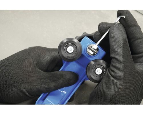 Nahaufnahme von Händen mit Arbeitshandschuhen, die eine blaue Fliesenschneidmaschine mit einem Inbusschlüssel einstellen.