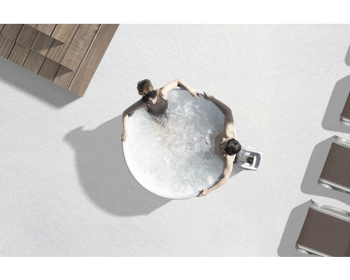 Draufsicht auf einen runden Whirlpool mit zwei Personen im Wasser, umgeben von Holzterrasse und Liegestühlen