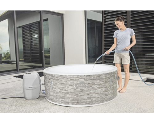 Frau füllt Lay-Z-Spa Vancouver auf, mit Steinmauer-Optik und Filterpumpe.