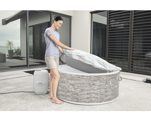 Frau öffnet den isolierenden Deckel eines Whirlpools mit Steinoptik im Freien