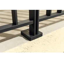 Detailaufnahme eines schwarzen Metallzauns mit Bodenbefestigung.