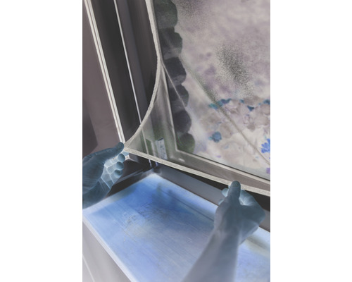 Une personne fixe une moustiquaire à une fenêtre.