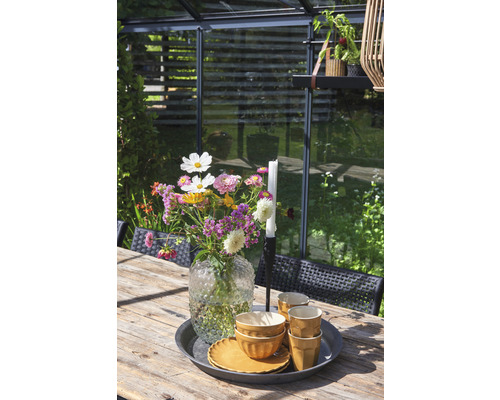 Table en bois dressée avec des fleurs, de la vaisselle et une bougie dans le jardin