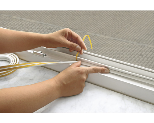 Eine Person bringt ein selbstklebendes Dichtungsband an einem Fenster an.