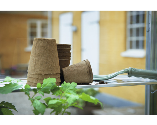 Anzuchttöpfe aus Zellulose mit Handrechen auf einem Regal