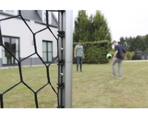 Detailansicht eines Fußballtors mit Netz und zwei spielenden Personen im Hintergrund