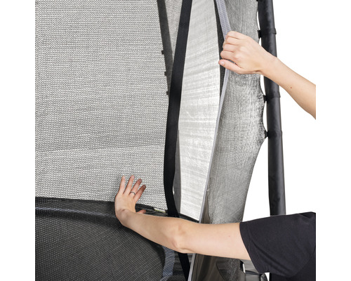 Gros plan d''un filet de sécurité de trampoline partiellement ouvert par deux mains pour dégager l''entrée