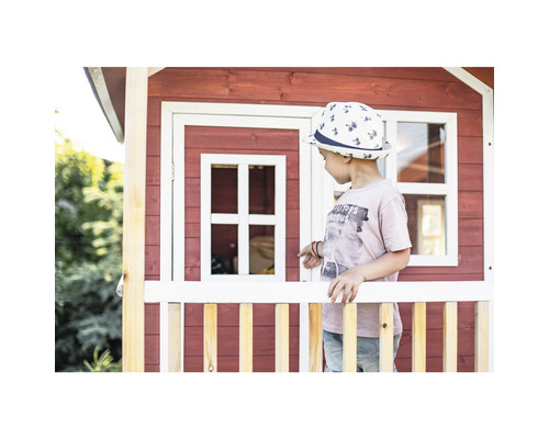Enfant devant une cabane de jeu en bois avec fenêtre et clôture
