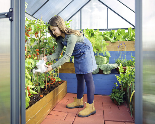 Eine Jugendliche giesst Tomatenpflanzen in einem Gewächshaus mit Salat- und Kräuterbeeten.