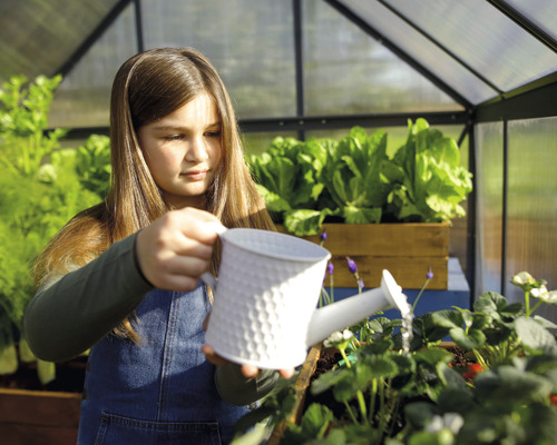 Ein Mädchen gießt Pflanzen in einem Gewächshaus mit einer Gießkanne.