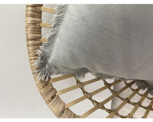 Coussin décoratif à franges sur fauteuil en rotin