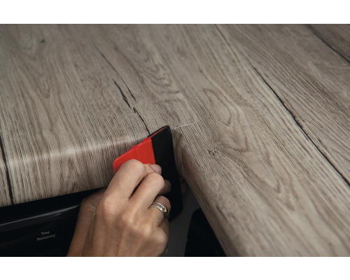 Person verwendet Werkzeug zum Anbringen von selbstklebender Holzdekorfolie