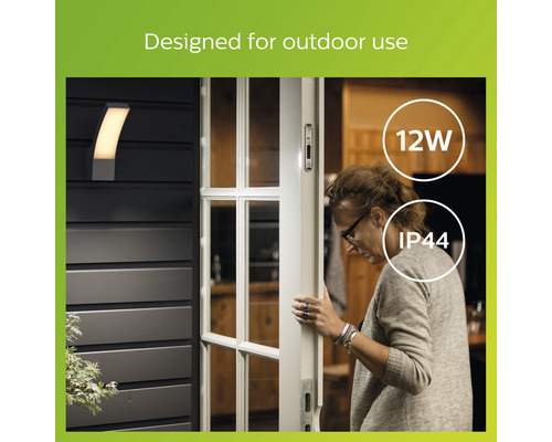 Eine Aussenwandleuchte neben einer Haustür, die eine Frau öffnet, gekennzeichnet mit 12 Watt und IP44 Schutzart.