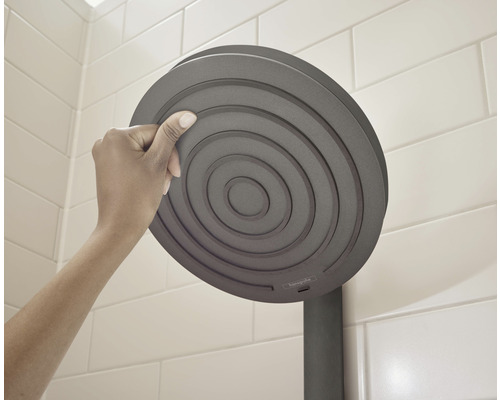 Une main touche une pomme de douche ronde dans une salle de bain