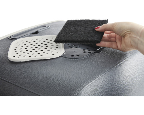 Eine Hand setzt einen Aktivkohlefilter in eine Katzentoilette ein.