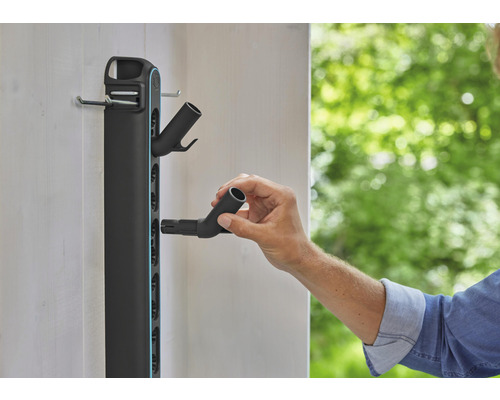 Support mural pour outils de jardin avec une personne fixant un raccord de tuyau