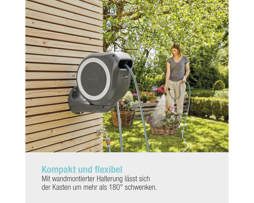 Gartenszene mit Schlauchbox an einer Holzwand und einer Frau, die Blumen gießt