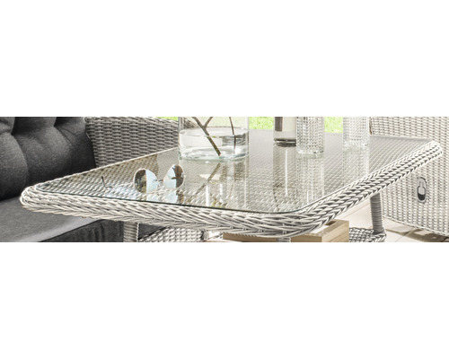 Nahaufnahme eines Gartentisches aus Rattan mit Glasplatte, auf dem eine Sonnenbrille und eine Vase stehen.