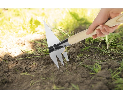 Hand hält eine Pendelhacke mit Holzstiel im Garten.