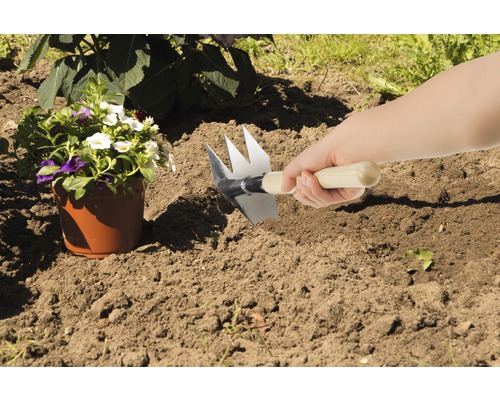 Szene mit einer Person, die ein Beet mit einer Gartenkralle vorbereitet, neben einem Blumentopf.