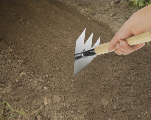 Nahaufnahme einer Person, die eine Pendelhacke mit Holzgriff im Garten verwendet.