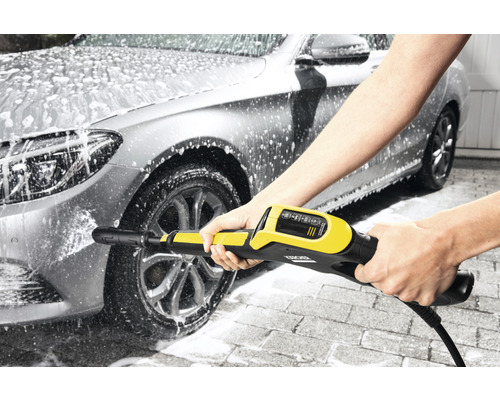 Une personne nettoie une voiture avec un nettoyeur haute pression.