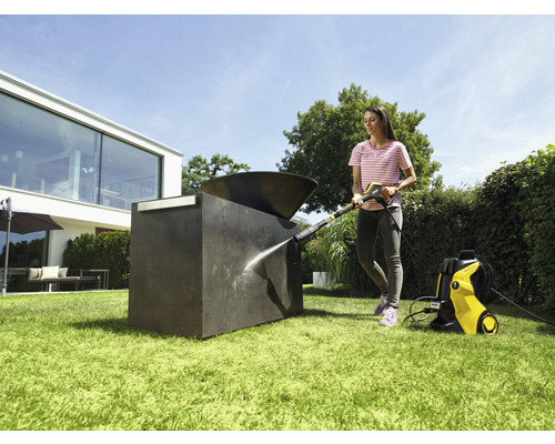 Femme nettoie une sculpture extérieure avec un nettoyeur haute pression dans le jardin.