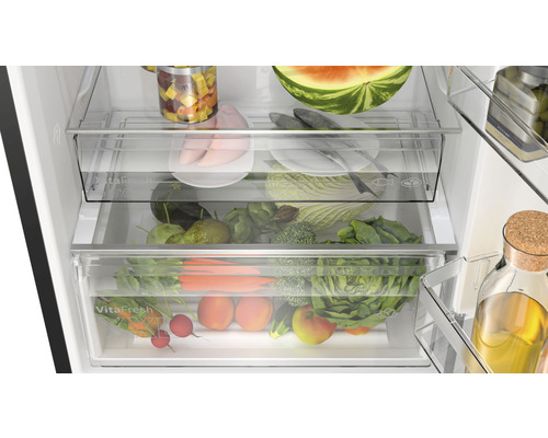 Innenraum eines Kühlschranks mit Gemüsefächern und verschiedenen Lebensmitteln wie Gemüse, Obst und Fleisch.
