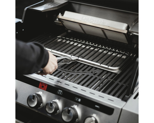 Person hantiert mit einer Grillzange im Innenraum eines Gasgrills