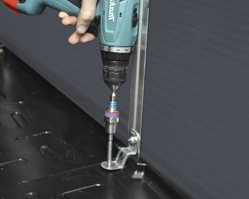 Eine Person schraubt mit einem Akkuschrauber eine Schraube in eine schwarze Oberfläche.