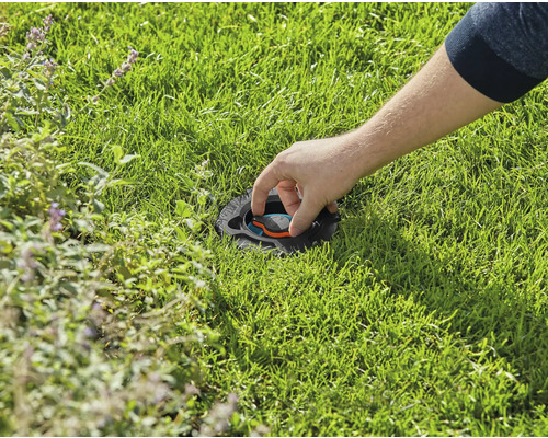Eine Person justiert einen versenkten Rasensprenger im Rasen.