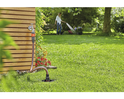 Gartenszene mit Wasserhahn, Gartenschlauch und Rasensprenger zur Bewässerung
