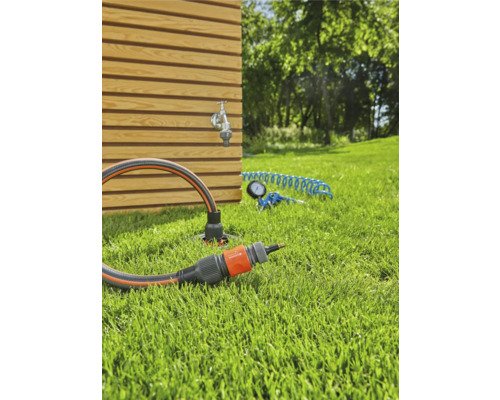 Gartenszene mit Wasserhahn, Gartenschlauch und Anschlussstück auf Rasen