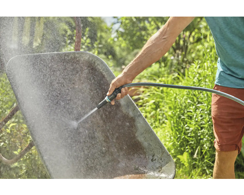 Eine Person reinigt eine Schubkarre mit einem Wasserschlauch im Garten.