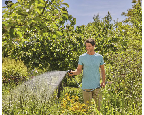 Homme arrosant le jardin avec un tuyau d''arrosage et une lance d''arrosage