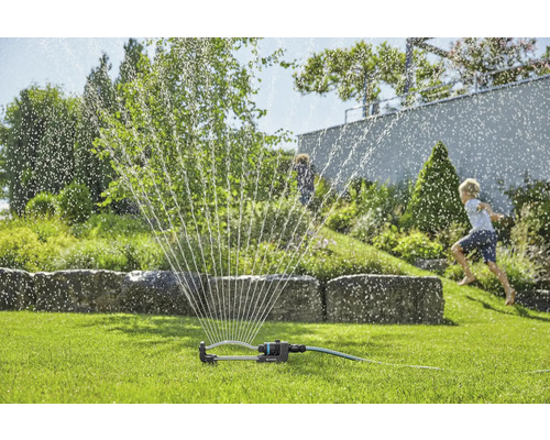 Rasensprenger im Betrieb auf einer Grünfläche mit spielenden Kindern im Hintergrund.