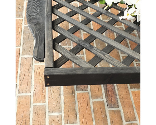 Detailansicht eines dunklen Spaliergitters aus Holz vor einer Ziegelwand