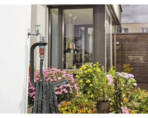 Gartenschlauch mit Halterung am Wasserhahn an einer Hauswand im Garten