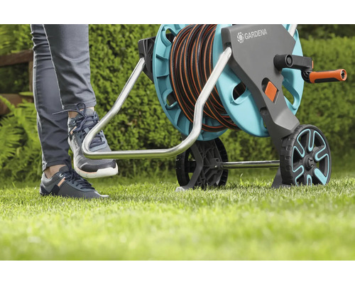 Gartenszene mit einer Person, die eine Gardena Schlauchtrommel mit dem Fuß bedient