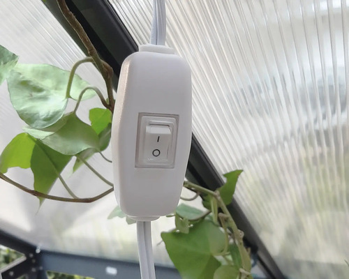 Ein weisser Schalter an einem Kabel, montiert in einem Gewächshaus.