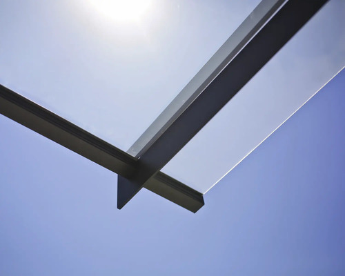 Detailansicht einer Terrassenüberdachung aus Glas und Metall vor blauem Himmel
