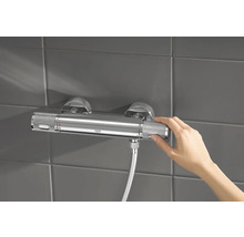 Mitigeur thermostatique apparent dans la salle de bains avec la main sur le régulateur de température