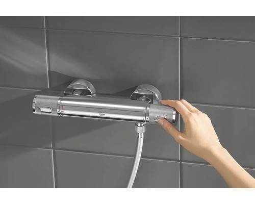 Mitigeur thermostatique apparent dans la salle de bains avec la main sur le régulateur de température