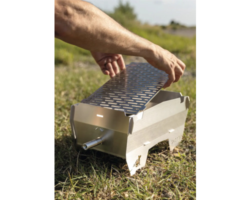 Person legt Grillrost auf einen tragbaren Grill