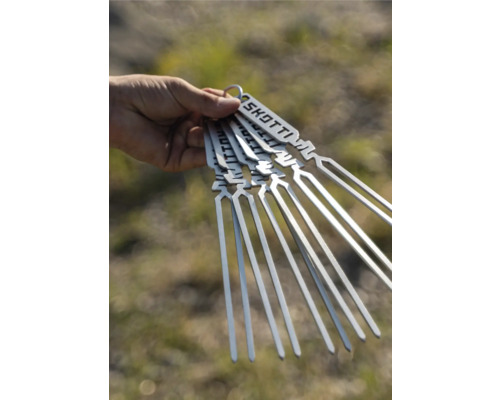 Eine Hand hält ein Set von Grillspießen aus Metall mit dem Skotti Logo.