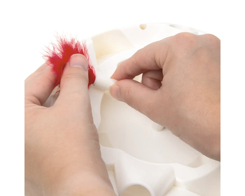 Une personne fixe une plume sur un jouet interactif pour chat.