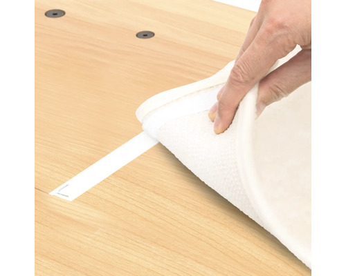 Hand befestigt einen Teppich mit Klettband auf einer Oberfläche.