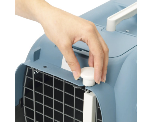 Vue détaillée d''une main actionnant une fermeture sur une caisse de transport pour animaux de compagnie.