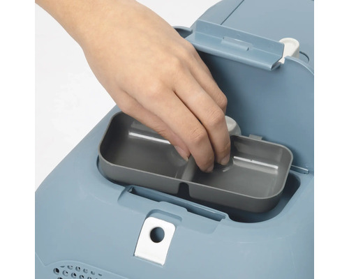 Detailaufnahme einer Hand, die einen Behälter in eine Katzentoilette einsetzt