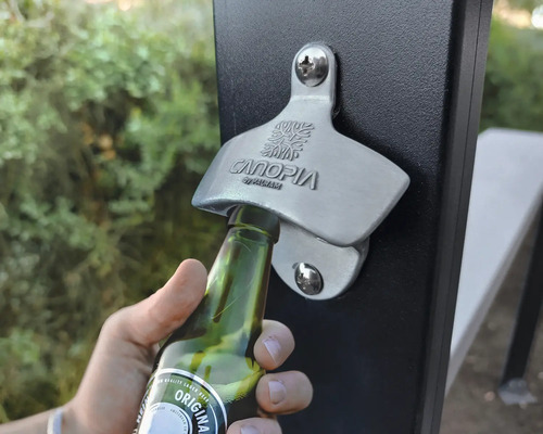 Aufnahme eines Flaschenöffners an einem Zaunpfosten, der zum Öffnen einer Glasflasche verwendet wird.